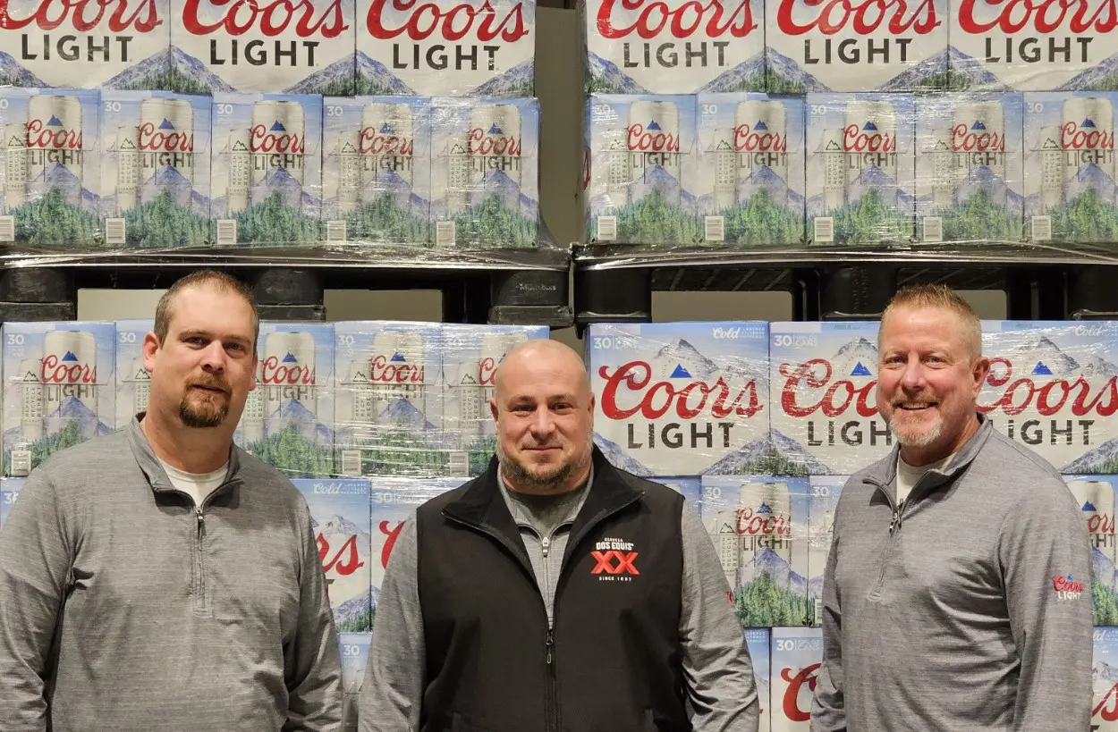 Three men standing in front of a wall full of coors light.